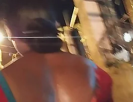 An Indian woman wears a backless sari and there is sweat all over her body in this outdoor scene.